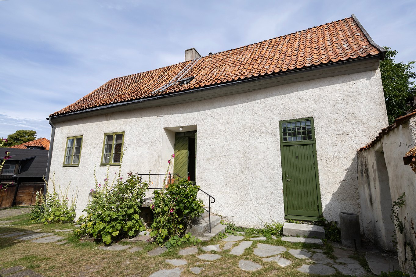 Vitkalkat hus med gröna dörrar och stockrosor